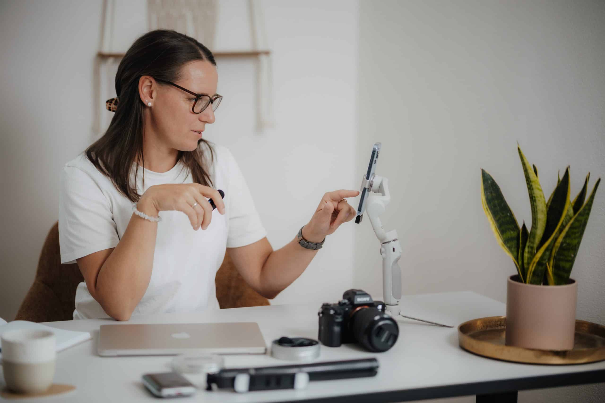 Daniela sitzt am Schreibtisch und filmt am Handy das auf einem Stativ steht