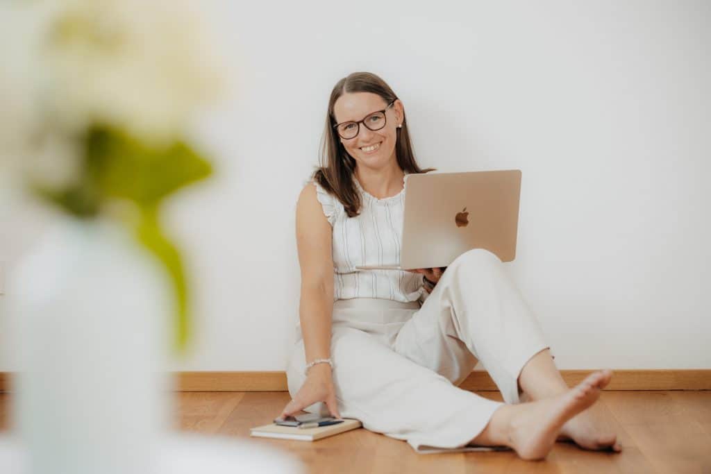 Daniela Neimer sitzt am Boden und lehnt an der Wand. Sie hat ihren Laptop in der Hand