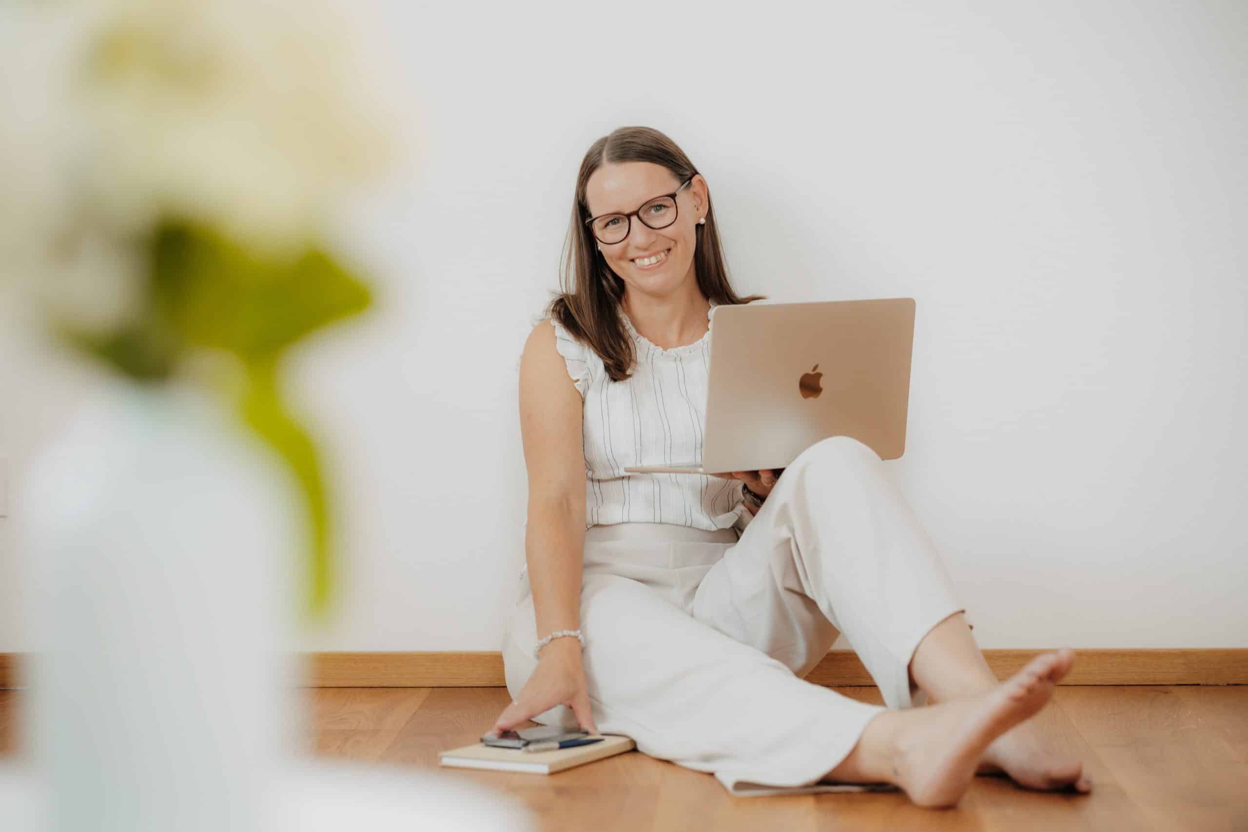 Daniela Neimer sitzt am Boden und lehnt an der Wand. Sie hat ihren Laptop in der Hand